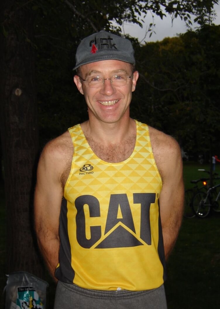 Jeff smiling with his arms behind his back in a bright yellow running tank with the Cat logo on the front.